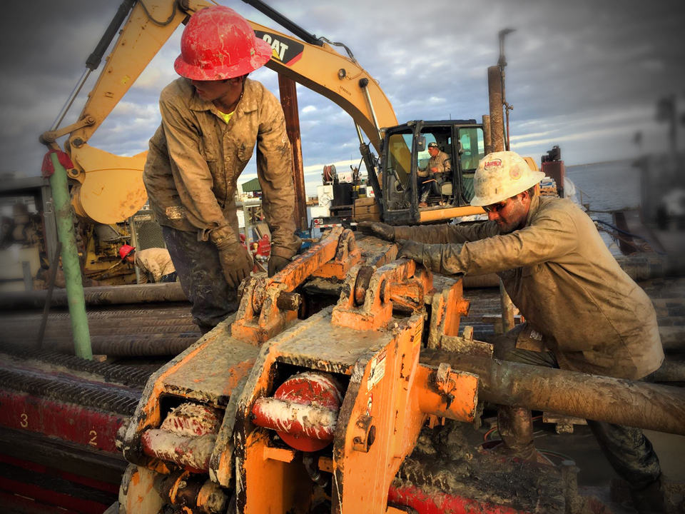 Two workers in hard hats with hands on HDD pipes