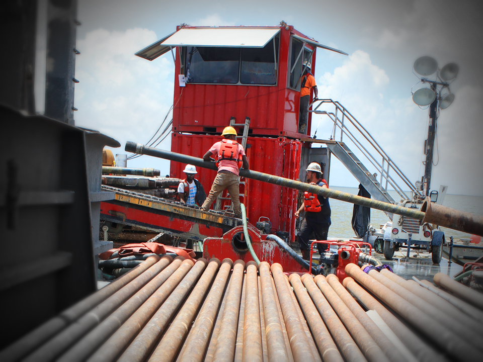 Worker in hard hat and life vest standing on stack of pipes on barge