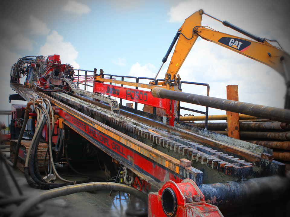 Large red HDD machine with yellow backhoe in background